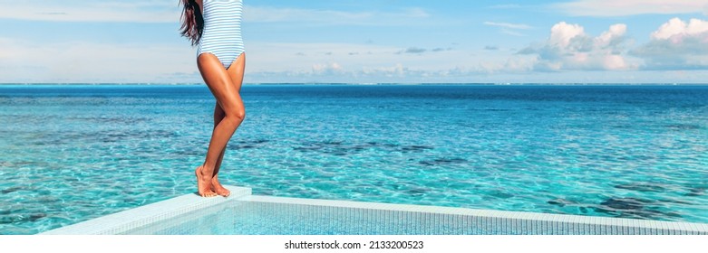 Summer tanned legs of swimsuit woman at infinity pool by the beach. Travel vacation banner panoramic of swimsuit model on blue ocean panorama. Luxury elegant lady holiday lifestyle.