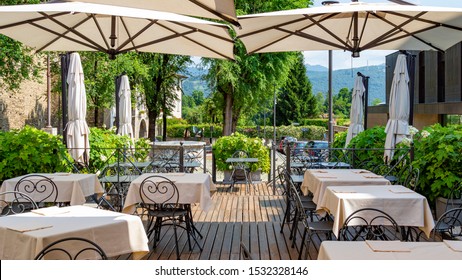 Summer terrace on the street. Old town. Cozy place in Italy. Outdoor tables and chairs of the restaurant, under awnings. Against the background of green Alps. Street cafe in Bergamo. No people.