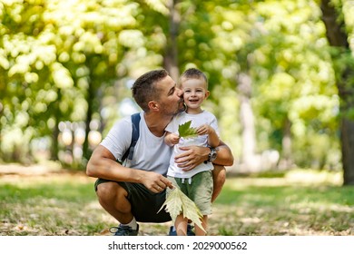 Summer Time For Family Fun In The Wood. Father And Son Dressed In The Same Clothes Fooling Around With Leaves Dad Squats Next To The Boy And Hugs And Kiss Him. Family Moments For Remember, Hiking