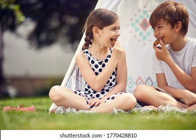 Summer Time Fun. Smiling Kids Playing At Backyard In Teepee And Eats Cookies. 
