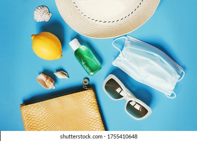 Summer Travel 2020 Accessories. Flat Lay Beach Essentials Cosmetic Bag, Alcohol Sanitizer Gel, Disposable Mask, Sunglasses, Sun Hat, Lemon And Seashells. Lifting Travel Bans