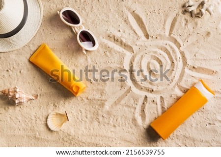 Summer travel beach flat lay composition, copy space. Hat, sunglasses, sunscreen lotion, sunblock cream  on beach sand background. Summer vacations and spf uv-protecting skin care concept.