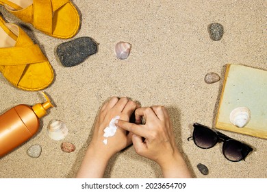 Summer And Travel Concept, Top View  Slippers, Body Cream And Sunglasses And Book On Sand, Woman Making Body Cream For Protect Her From The Sun