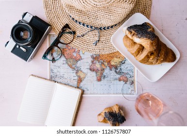 Summer Travel Flat Lay: World Map, Vintage Film Camera, Croissant, A Glass Of Rose Wine, Wicker Beach Hat, Paper Notepad, Glasses On The Pink Wooden Table Background, Top View, Flat Lay