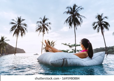 Summer Travel Vacation Concept, Happy Traveler Asian Woman With Bikini Relax On Pool Float In Luxury Infinity Pool Hotel Resort With Sea Beach And Palm Tree Background At Sunset In Koh Kood, Thailand