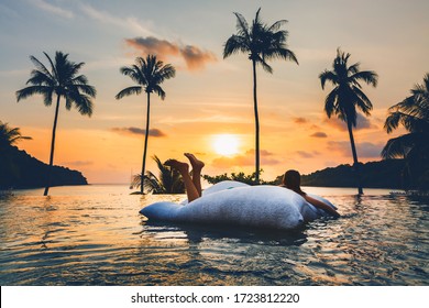 Summer Travel Vacation Concept, Happy Traveler Asian Woman With Bikini Relax On Pool Float In Luxury Infinity Pool Hotel Resort With Sea Beach And Palm Tree Background At Sunset In Koh Kood, Thailand