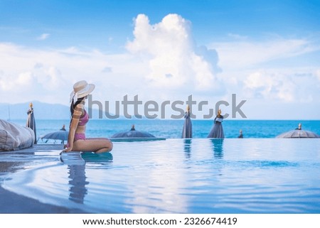 Summer travel vacation concept, Happy traveler asian woman with hat and bikini relax in luxury infinity pool hotel resort at day in Koh Samui, Surat Thani, Thailand