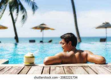 Summer Travel Vacation Concept, Traveler Asian Man With Coconut Relax In Luxury Infinity Pool Hotel Resort With Sea Beach And Palm Tree Background 