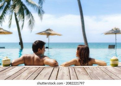 Summer Travel Vacation Concept, Traveler Asian Couple  With Coconut Relax In Luxury Infinity Pool Hotel Resort With Sea Beach And Palm Tree Background 