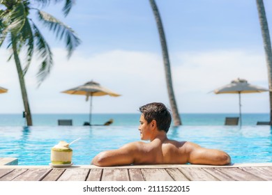 Summer Travel Vacation Concept, Traveler Asian Man With Coconut Relax In Luxury Infinity Pool Hotel Resort With Sea Beach And Palm Tree Background 