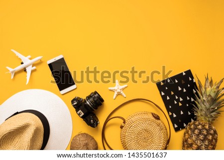 Summer traveler accessories flat lay. Straw hat, retro film camera, bamboo bag, sunglasses, coconut, pineapple, sea shells and starfish, air plane, notebook and phone over yellow background, top view.