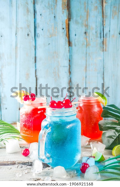 Summer tropical cold drinks. Blue Hawaiian, Tequila\
sunrise, Sea breeze cocktails over light blue wooden beach\
background, copy space
