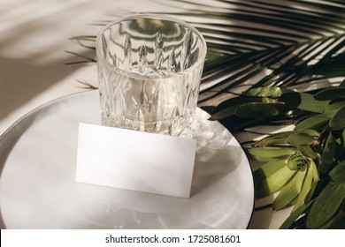 Summer Tropical Stationery Still Life Scene. Glass Of Water, Palms Leaves, Leucadendron Flower. Beige Table Background In Sunlight. Blank Business, Greeting Card, Invitation Mockup Scene. Long Shadows