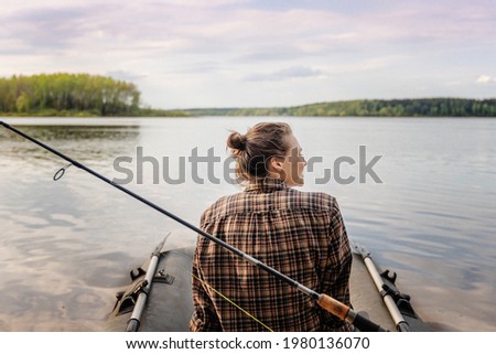 Summer vacation and activity. Young beautiful woman sailing on an inflatable boat with a fishing rod on a summer forest lake