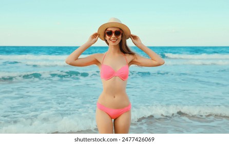 Summer vacation, beautiful happy lovely woman in pink bikini swimsuit, tourist straw hat, red heart shaped glasses on the beach on sea coast with waves - Powered by Shutterstock