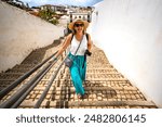 Summer vacation. Beautiful young woman in flowing fashionable clothes with camera walking up stairs and sightseeing the old city of Tavira Portugal on a sunny summer day. Visit the old town of Tavira