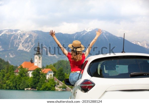 Summer vacation car road trip
freedom concept. Happy woman cheering joyfuly by rising hands to
the sky enjoying beautiful view of lake Bled, Slovenia,
Europe.