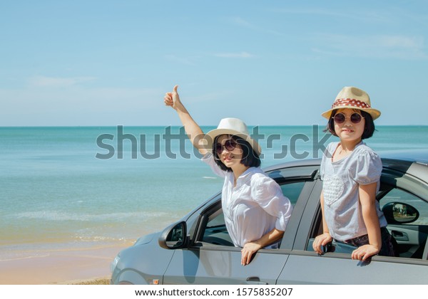 Summer\
Vacation and Car Trip Concept : Family car trip at the sea, Woman\
and child cheerful raising their hands up and feeling happiness in\
silver car with seascape in the\
background.