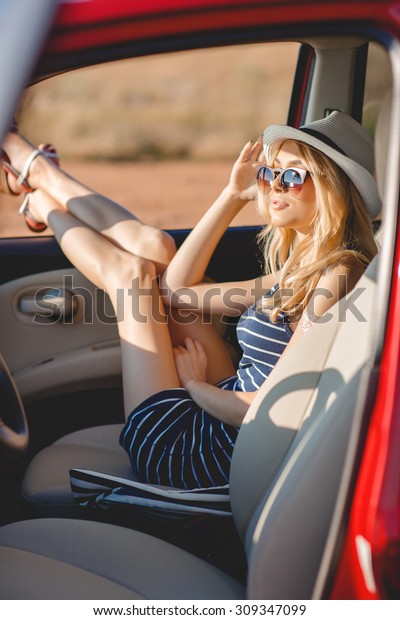Summer vacation. Car trip. Travelling. Car travel. By\
the sea. Beautiful blonde woman standing with red small car on the\
background. Sea style. Summer vacation car road trip freedom\
concept. 