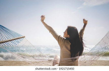Summer vacation concept, Cheerful asian female tourist stretch arms relaxing sitting on hammock at beautiful beach