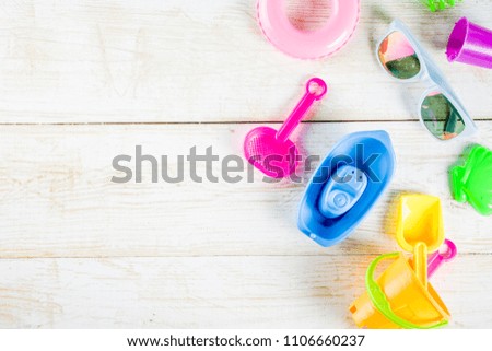 Summer vacation concept with plastic beach kids toys - bucket, scoop, rake, molds boat, lifebuoy toys copy space white wooden background above