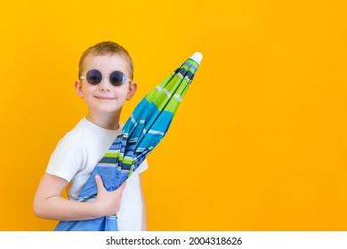 Summer Vacation Concept, Portrait Of Happy Cute Little Child, Boy With Glasses Smiling And Holding A Beach Umbrella, Studio Shot Isolated On Yellow Background