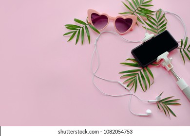 summer vacation concept. stylish pink sunglasses, phone on selfie stick, headphones, and green palm leaves on pink background, flat lay.  space for text. time to travel
