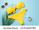 Summer vacation concept. Top view photo of gold rings bracelet stylish sunglasses yellow bikini and palm leaves on isolated pastel blue background