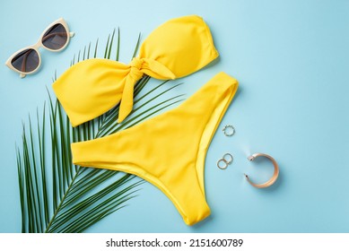 Summer vacation concept. Top view photo of gold rings bracelet stylish sunglasses yellow bikini and palm leaves on isolated pastel blue background