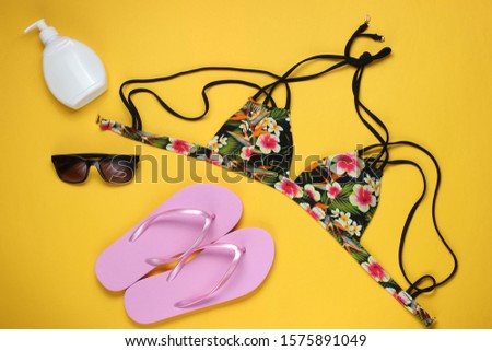 Summer vacation concept. Woman's swimsuit bikini, flip flops and beach accessories on yellow background. Overhead view of woman's swimwear. Flat lay, top view. 