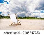 Summer vacation. Empty deckchair standing on white sand beach. Trees in distance. Relaxation and peace by sea. Unfolded deckchair inviting you to sunbathe and rest and read books