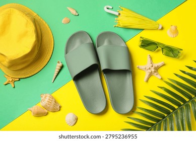 Summer vacation essentials flat lay with green slides, yellow hat, sunglasses, umbrella, seashells, and palm leaf