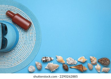 Summer and vacation flat lay with a beauty blue striped woman straw hat, sun glasses, Suntan oil and various seashells at the lower edge of the picture on blue background.