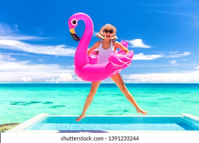 Summer vacation fun funny woman jumping with flamingo swimming pool float around waist excited of tropical hotel holiday.