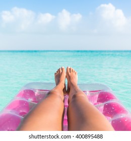 Summer vacation girl lower body closeup. Woman tanning legs  relaxing in ocean on pink inflatable swimming pool air mattress bed floating in turquoise water background. Suntan at tropical beach.