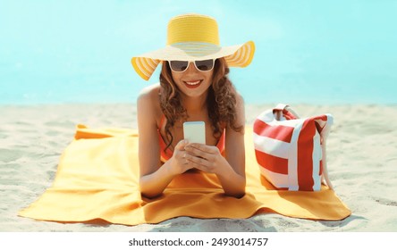 Summer vacation, happy young woman with phone, tourist hat, beautiful girl holding smartphone lying on the sand on the beach on sea background - Powered by Shutterstock