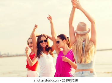 summer vacation, holidays, travel and people concept - group of smiling young women in sunglasses and casual clothes dancing on beach