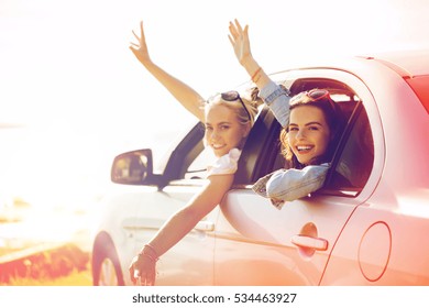 Summer Vacation, Holidays, Travel, Road Trip And People Concept - Happy Teenage Girls Or Young Women In Car At Seaside Waving Hands