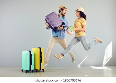 Summer Vacation Hype. Happy Overjoyed Young Caucasian Family Couple Jumping With Travel Accessory Looking At Each Other Funny Studio Full Body Portrait. In Anticipation Of Travel, Rest And Adventure