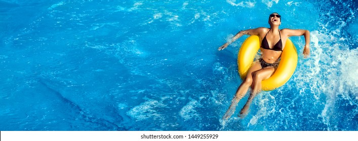 Summer Vacation, Laughing Young Woman Enjoying An Aqua Park With A Yellow Float On Sparkling Blue Water In A Pool With Turbulence And Copy Space In An Overhead Panorama