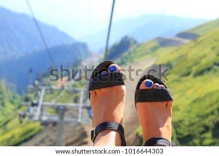 Summer vacation. Legs in sandals with a pedicure above the abyss, the girl goes by cable way in the mountains. Summer active rest