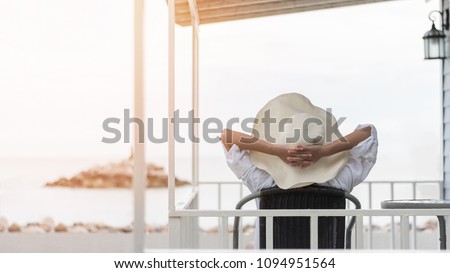 Summer vacation lifestyle with young girl wearing sunscreen hat on sunny day relaxing taking it easy happily sitting on the porch at beach-house on beach front celebrating healthy living life quality