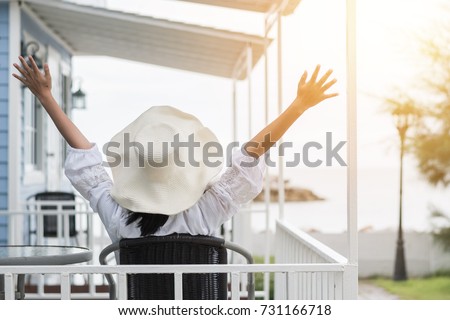 Summer vacation lifestyle with young girl wearing sunscreen hat on sunny day relaxing taking it easy happily sitting on the porch at beach-house on beach front celebrating healthy living life quality
