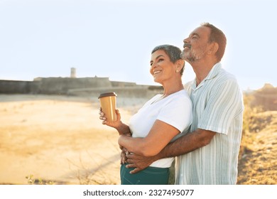 Summer Vacation. Loving Mature Husband Embracing Wife From Back Standing At Sea Coastline Outside, Side View Shot With Copy Space. Spouses With Coffee Cup Enjoying Weekend At Ocean - Powered by Shutterstock