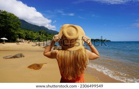Summer vacation on tropical island. Panoramic banner view of young woman holding straw hat on the sand beach.