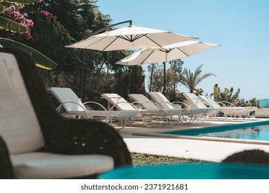 Summer vacation at poolside. Veranda decorated with deck chairs and umbrella with an ocean view - Shutterstock ID 2371921681