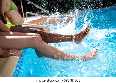 Summer Vacation At Resort With Friends. Closeup Of Young People Having Fun Together, Sitting Near Swimming Pool And Dangling Feet In Blue Water On Summer Day Outdoors