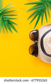 Summer Vacation, Resort Theme. White Bucket Hat With Black Sun Glasses On Yellow Sunny Background With Green Palm Leaves. Flat Lay, Top View