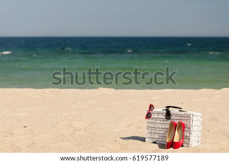 Summer vacation at sea. White wicker suitcase and women's accessories and shoes on the beach. Selective focus.