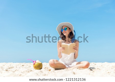 Summer Vacation. Smelling tourist 
 asian women relaxing and reading book with sunglasses in beach, happy and tranquility luxury holiday sunny, outdoors blue sky background. Travel lifestyle Concept.